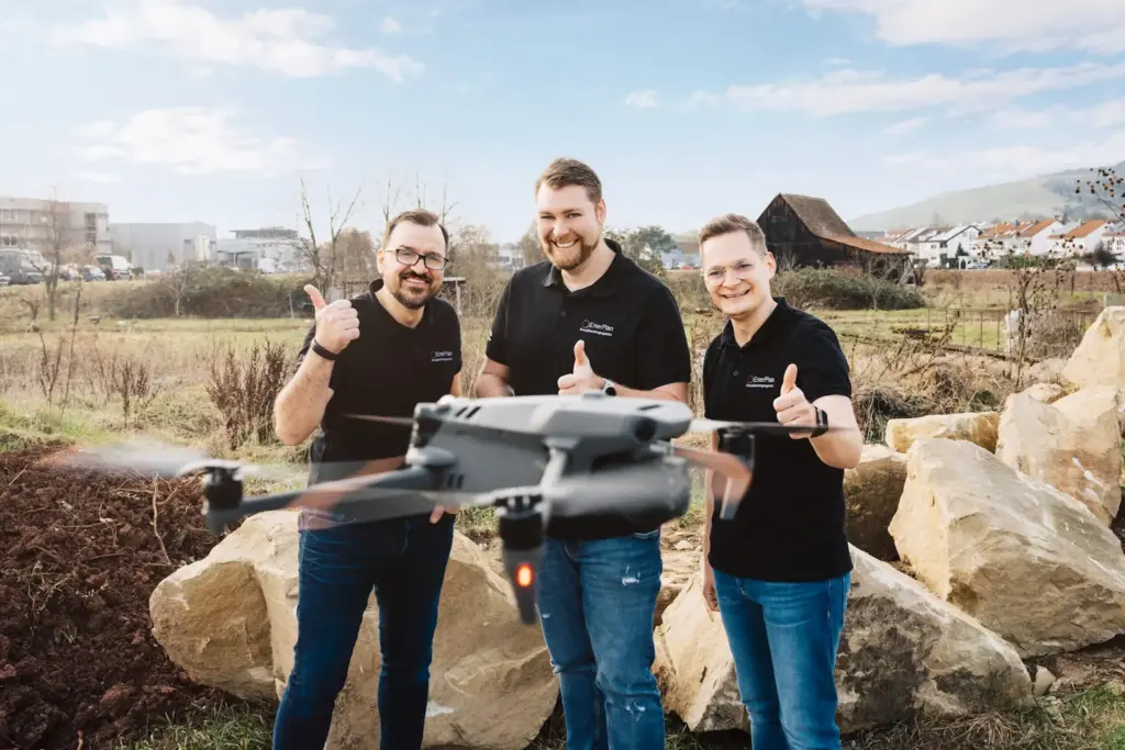Die drei Geschäftsführer von EnerPlan stehen vor einer Landschaft. Alle zeigen den Daumen nach oben. Vor ihnen fliegt eine Drohne.